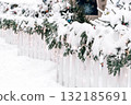 Snow-covered white fence adorned with evergreen garlands and twinkling lights for Christmas ambiance 132185691