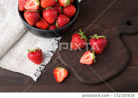 Beautiful ripe strawberry on the table. Studio shot of red strawberry berries on dark table with cutting board and white towel Beautiful ripe strawberry on the table. Studio shot of red strawberry berries on dark table with cutting board and white towel 132185816