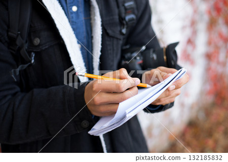 Young boy with notebook and pencil making sketches. Male enthusiast photographer in the park searching for inspiration. Young boy with notebook and pencil making sketches. Male enthusiast photographer in the park searching for inspiration. 132185832