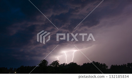 Three thunder lightnings over trees at night. Dramatic photo of lightnings during the rain 132185834