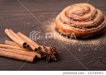 Sticks of cinnamon on the foreground and heavily flavoured cinnamon bun in the background. Baking concept Sticks of cinnamon on the foreground and heavily flavoured cinnamon bun in the background. Baking concept 132185851