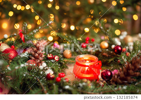 Close up shot of red burning candle in christmas wreath with bright colorful background. Festive Christmas mood Close up shot of red burning candle in christmas wreath with bright colorful background. Festive Christmas mood 132185874