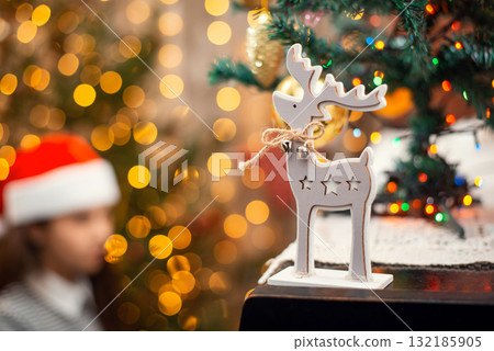 Wooden deer as Christmas symbol standing on the piano, atmosphere of the holidays. Bright lights, festive decoration and female pianist on the background. Wooden deer as Christmas symbol standing on the piano, atmosphere of the holidays. Bright lights, festive decoration and female pianist on the background. 132185905