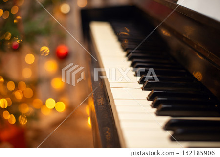 Keys of the piano close up, festive Christmas decoration and lights on the background. Entertainment on holidays, musical accompaniment concept. Keys of the piano close up, festive Christmas decoration and lights on the background. Entertainment on holidays, musical accompaniment concept. 132185906