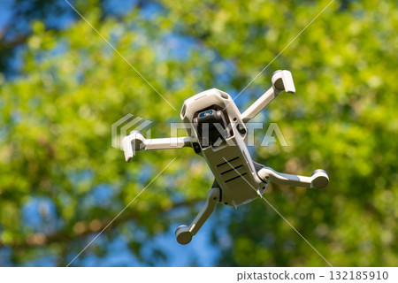 Bottom view of a little drone against green trees. Modern technology, RC aircraft, filming video and shooting stills Bottom view of a little drone against green trees. Modern technology, RC aircraft, filming video and shooting stills 132185910
