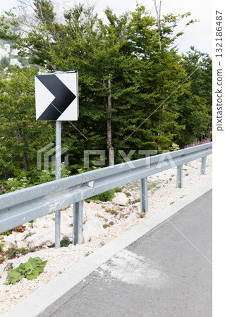 A bold right-pointing road sign stands near a metal guard rail A bold right-pointing road sign stands near a metal guard rail 132186487