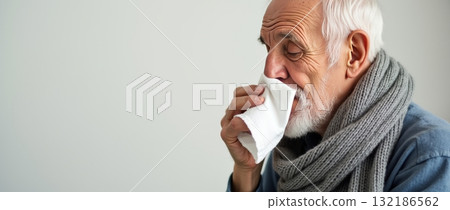 Elderly man with a scarf using a tissue, light background, concept of cold, flu, or seasonal illness. Common cold concept. Copy space. 132186562