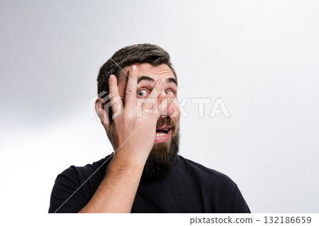 Man peeking through fingers with surprised expression. 132186659