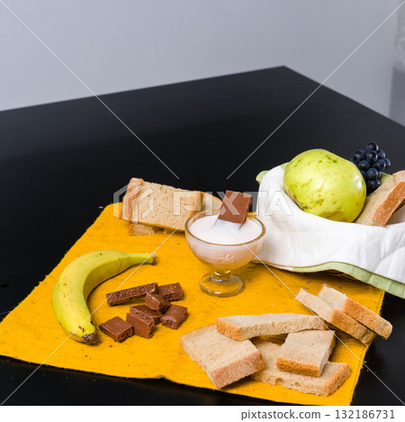 Simple breakfast spread with fruit, bread, yogurt, and chocolate. 132186731