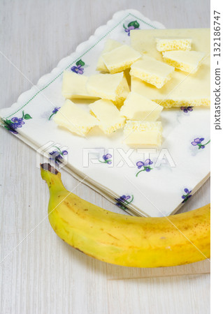 White chocolate pieces and a banana on a table. White chocolate pieces and a banana on a table. 132186747
