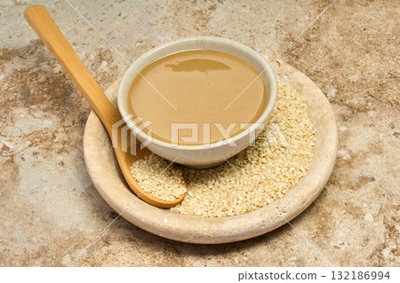 Sesame Tahini Bowl. A bowl of creamy tahini with sesame seeds on a rustic travertine surface. Sesame Tahini Bowl. A bowl of creamy tahini with sesame seeds on a rustic travertine surface. 132186994