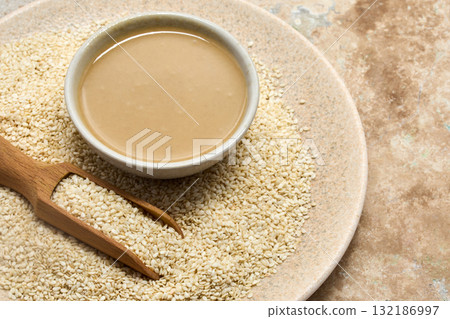Sesame and Tahini Harmony. A bowl of creamy tahini beside a scoop of sesame seeds on a stone plate. Sesame and Tahini Harmony. A bowl of creamy tahini beside a scoop of sesame seeds on a stone plate. 132186997