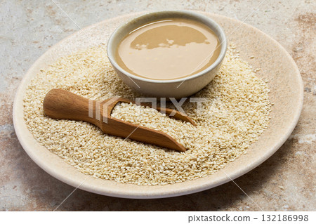 Sesame and Tahini Harmony. A bowl of creamy tahini beside a scoop of sesame seeds on a stone plate. Sesame and Tahini Harmony. A bowl of creamy tahini beside a scoop of sesame seeds on a stone plate. 132186998