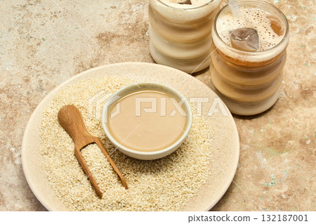 Sesame Tahini Latte Delight. Creamy sesame paste and iced tahini lattes on rustic travertine surface. 132187001