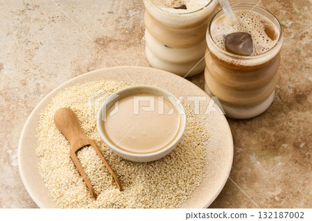 Sesame Tahini Latte Delight. Creamy sesame paste and iced tahini lattes on rustic travertine surface. 132187002