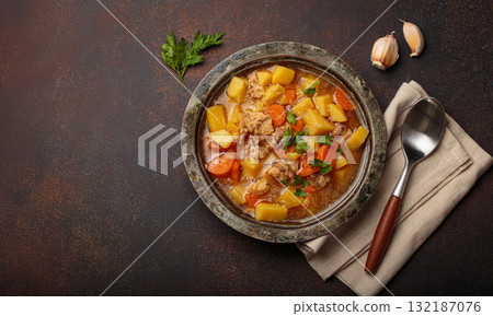 Chicken stew or soup with potatoes and carrots served in rustic bowl with spoon top view on dark brown concrete background, space for text 132187076