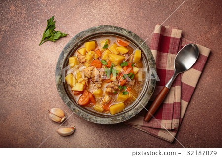 Chicken stew or soup with potatoes and carrots served in rustic bowl with spoon top view on dark brown concrete background 132187079