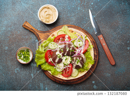 Preparing and cooking falafel wrap on pita on wooden cutting board with hummus top view 132187080