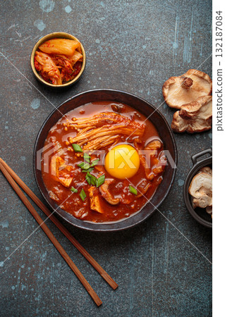 Traditional Korean kimchi jjigae hot soup or stew with egg yolk in black rustic bowl on dark background top view 132187084