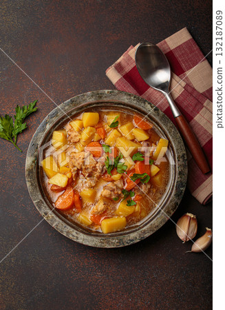 Chicken stew or soup with potatoes and carrots served in rustic bowl with spoon top view on dark brown concrete background 132187089