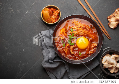 Traditional Korean kimchi jjigae hot soup or stew with egg yolk in black rustic bowl on dark background top view, space for text 132187105