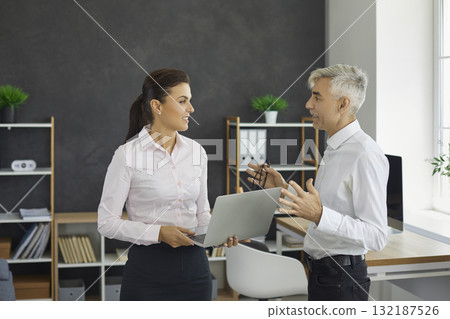 Senior boss chief giving advice to young employee standing with laptop in office 132187526