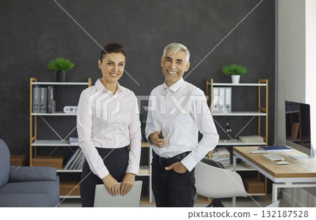 Senior male boss and young female secretary standing in office portrait 132187528