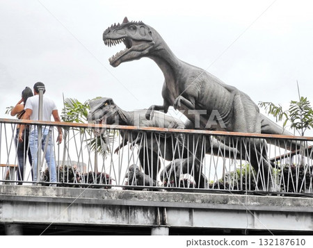Two people stand on an outdoor platform with large, lifelike dinosaur sculptures looming behind them Two people stand on an outdoor platform with large, lifelike dinosaur sculptures looming behind them 132187610