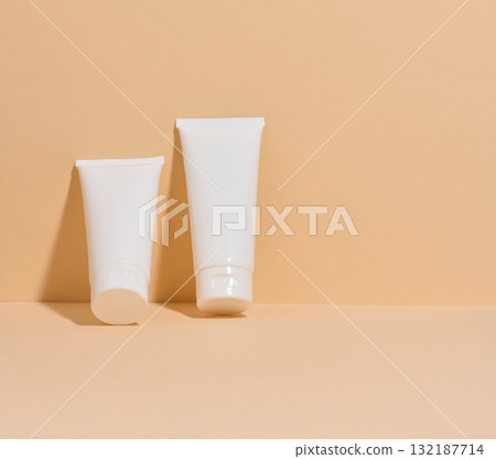 Two white cosmetic tubes without markings on a minimalist beige background. 132187714
