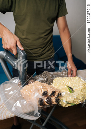 Vertical cropped shot of man using vacuum cleaner to suck air out of plastic bags containing plush toys, placed on ironing board, for efficient storage and space saving. Concept of household chores. Vertical cropped shot of man using vacuum cleaner to suck air out of plastic bags containing plush toys, placed on ironing board, for efficient storage and space saving. Concept of household chores. 132187946