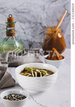 Delicious miso soup with noodles and broccoli in a bowl on the table vertical view Delicious miso soup with noodles and broccoli in a bowl on the table vertical view 132188029
