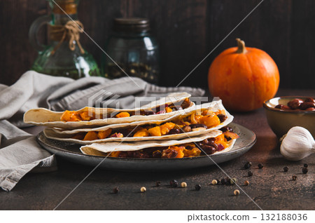 Delicious tacos with baked pumpkin, beans and cheese on a plate on the table Delicious tacos with baked pumpkin, beans and cheese on a plate on the table 132188036