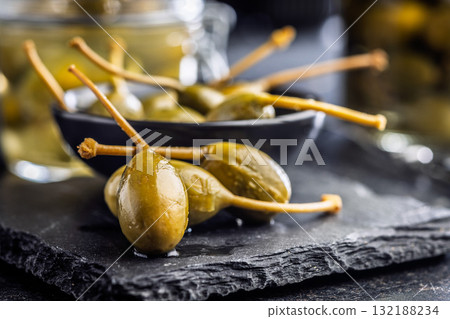 Pickled capers berries on black table. Pickled capers berries on black table. 132188234