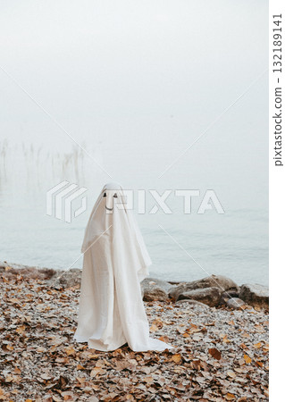 little child dressed up as a ghost standing on the beach of the lake little child dressed up as a ghost standing on the beach of the lake 132189141