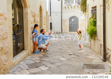 father with elder daughter taking photo with mobile photo of smaller daughter on narrow street father with elder daughter taking photo with mobile photo of smaller daughter on narrow street 132189148