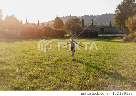 high angle view of a small happy girl running on the field in the evening with stretched arms 132189152
