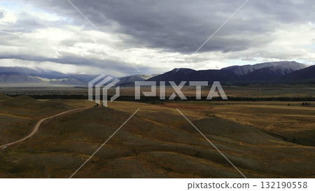 Vast mountain valley landscape showing dirt road and cloudy sky. Media Vast mountain valley landscape showing dirt road and cloudy sky. Media 132190558
