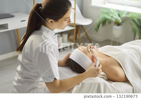 Esthetician performing facial treatment with handheld device in spa salon 132190673