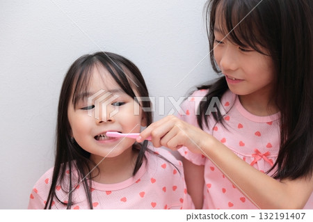 Two sisters, ages 4 and 10, brushing their teeth in pajamas 132191407