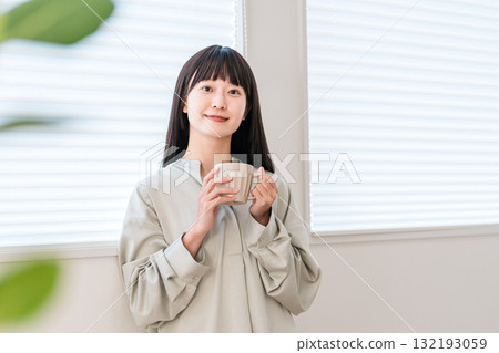 年輕的亞洲女性一邊在窗邊喝熱飲、茶或咖啡,一邊看著智慧型手機 年輕的亞洲女性一邊在窗邊喝熱飲、茶或咖啡,一邊看著智慧型手機 132193059