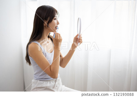 一位年輕女子拿著手鏡刷牙 132193088