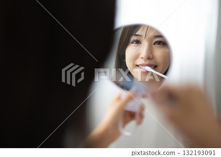 一位年輕女子拿著手鏡刷牙 132193091