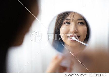 一位年輕女子拿著手鏡刷牙 132193092