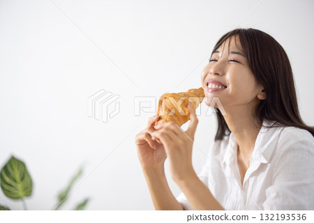 Smiling young woman eating a croissant Smiling young woman eating a croissant 132193536