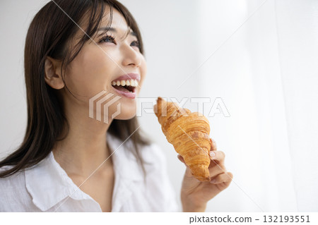Smiling young woman eating a croissant 132193551