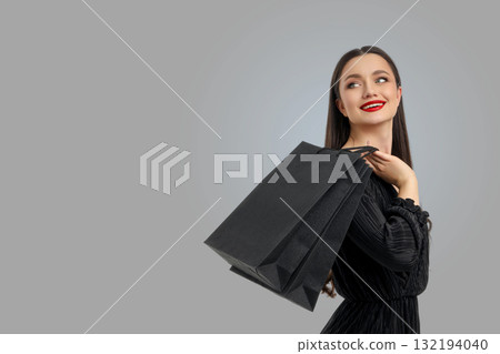 Woman wearing black dress holding shopping bags and smiling 132194040