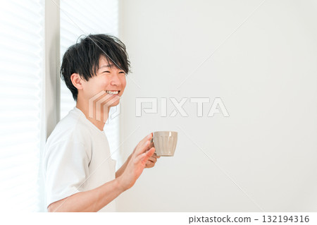 Young Asian man greeting someone by the window with a hot drink, tea, or coffee 132194316