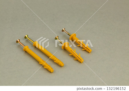 Different types of yellow wall anchors and screws on a neutral background 132196152
