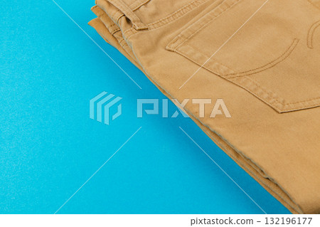 Casual tan pants folded neatly on a vibrant blue background Casual tan pants folded neatly on a vibrant blue background 132196177