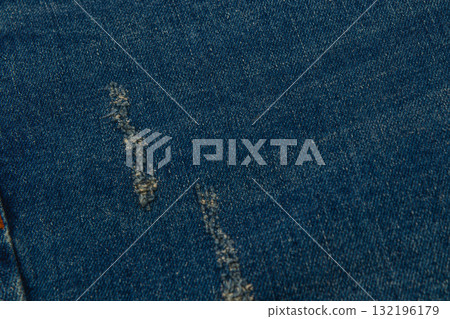 Denim fabric with noticeable wear and tear features a deep blue color Denim fabric with noticeable wear and tear features a deep blue color 132196179